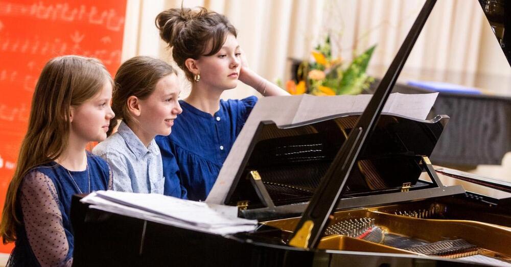 Drei Kinder sitzen vor einem Klavier.