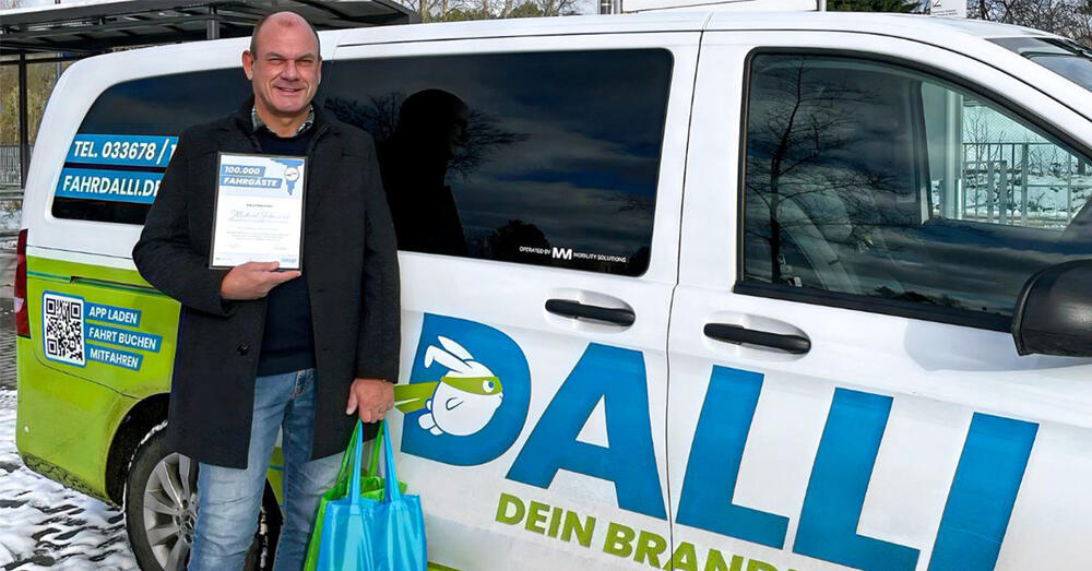 Der 100.000. Fahrtgast steht vor einem Dalli-Bus und h&auml;lt eine Urkunde in der Hand.