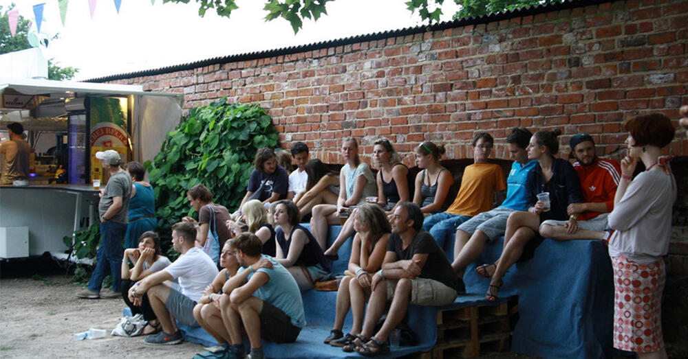 G&auml;ste des Musikfestivals "Jenseits von Millionen" in Friedland sitzen auf B&auml;nken und verfolgen gespannt einen Auftritt.